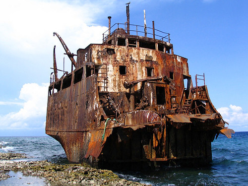 A rusting shipwreck on rocks by the sea